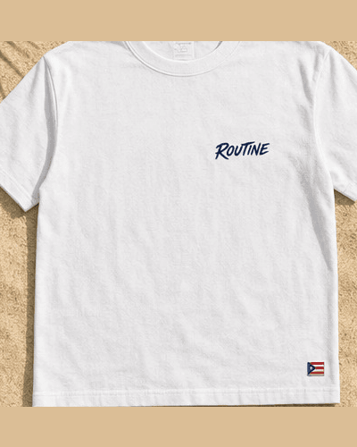 Front of the white La Isla beach tee with a small navy ROUTINE script and a flag tag at the hem.