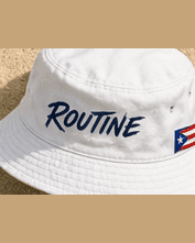 White La Isla bucket hat with a navy ROUTINE script.