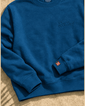 Ocean blue La Isla crewneck with a tonal ROUTINE script and a small flag tag on the cuff.