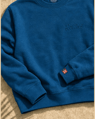 Ocean blue La Isla crewneck with a tonal ROUTINE script and a small flag tag on the cuff.
